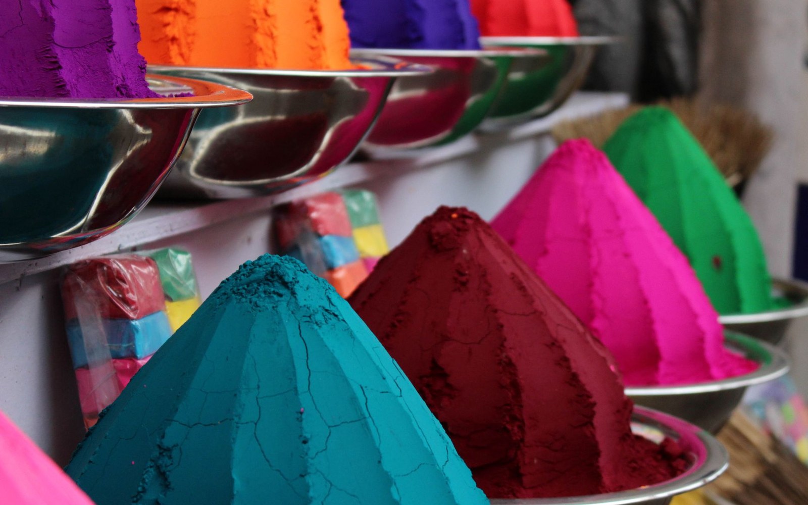 Cone-shaped mounds of colored pigment powder displayed in metal bowls on shelves