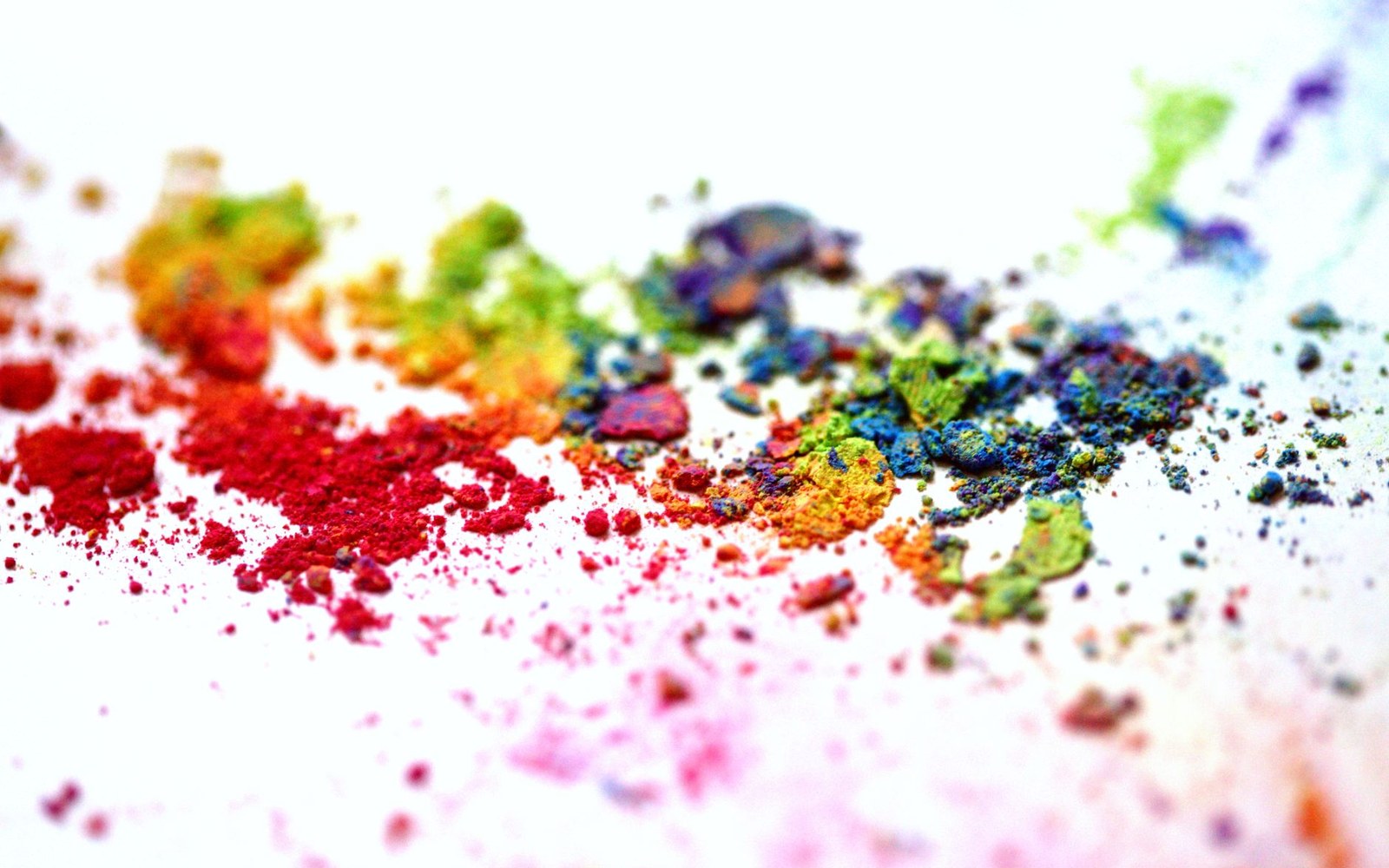 Scattered rainbow-colored pigment powders blending across a white surface