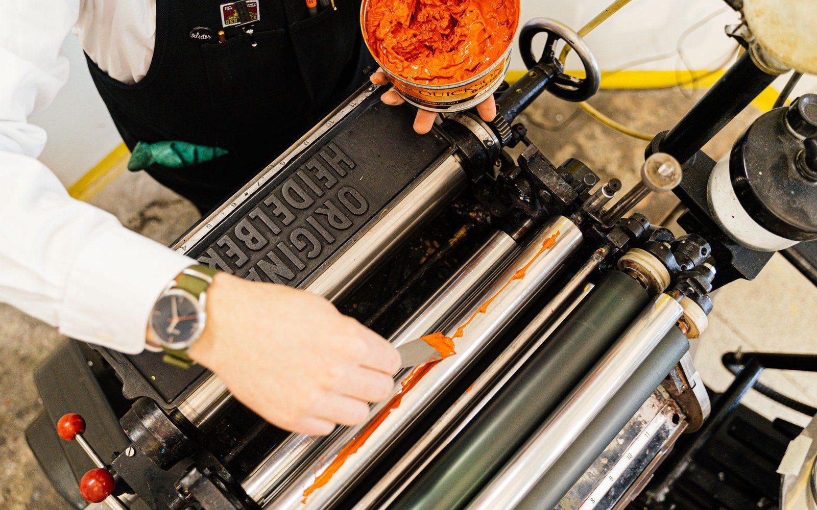A printer applies orange ink to the rollers of an original Heidelberg press