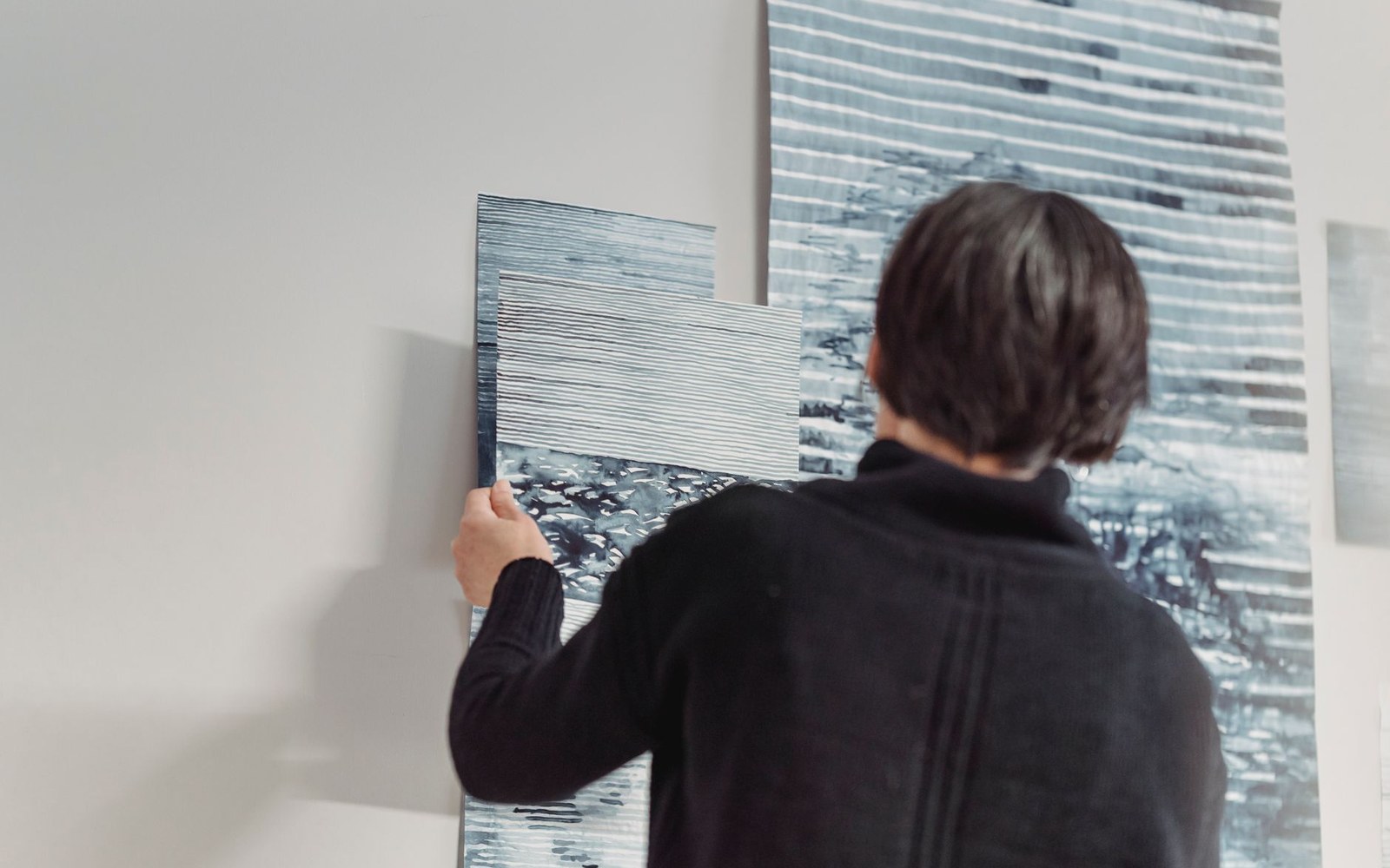 A person examines abstract striped artworks pinned to a gallery wall