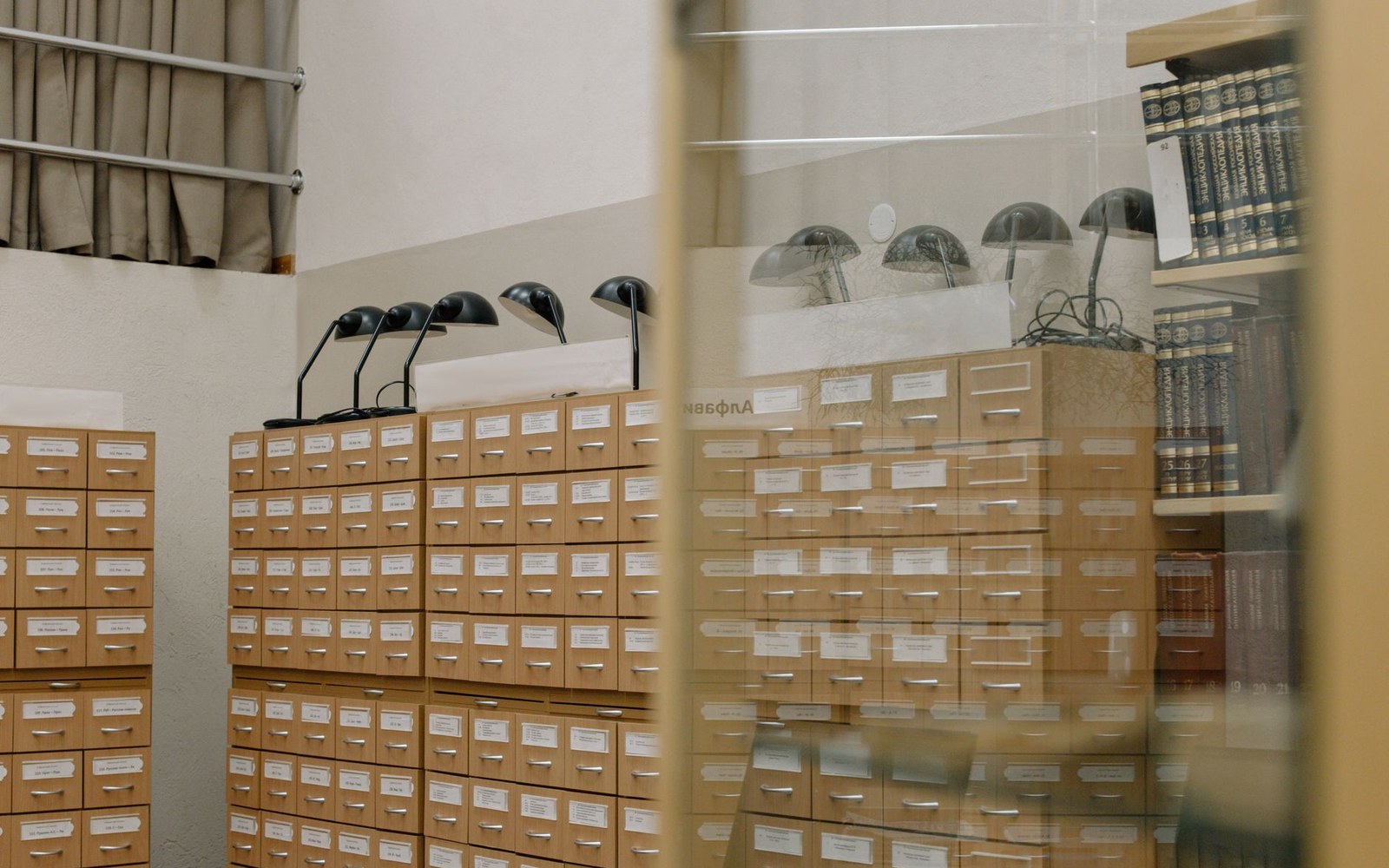 Rows of wooden card catalog drawers topped with desk lamps in a library