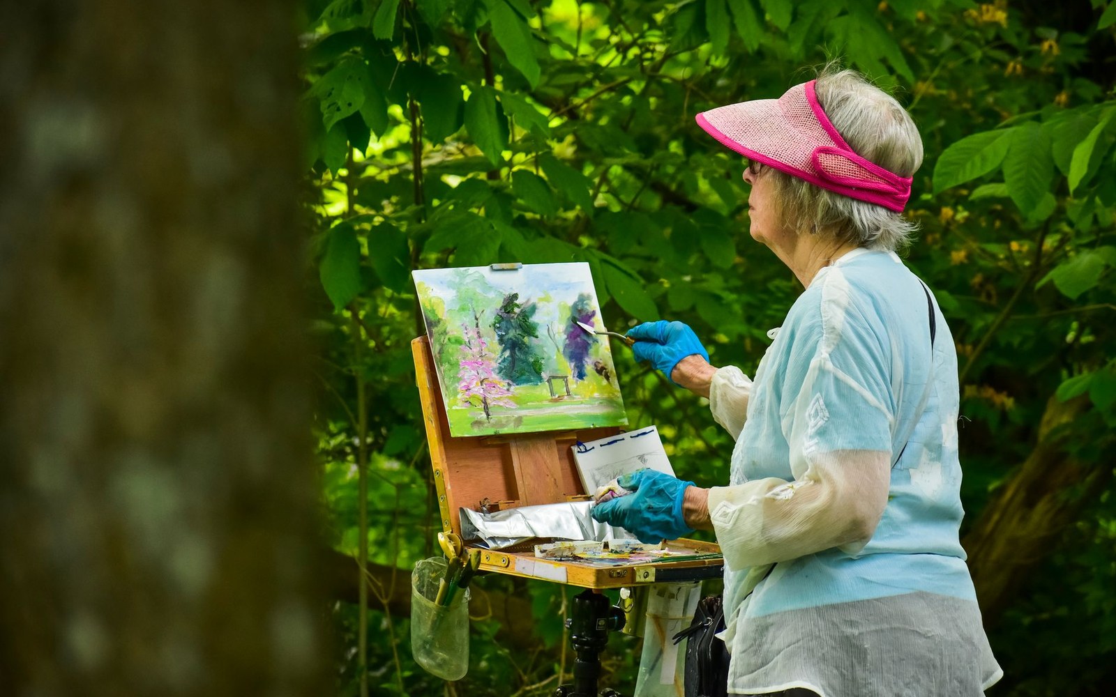 A woman in a visor paints a landscape on a portable easel outdoors