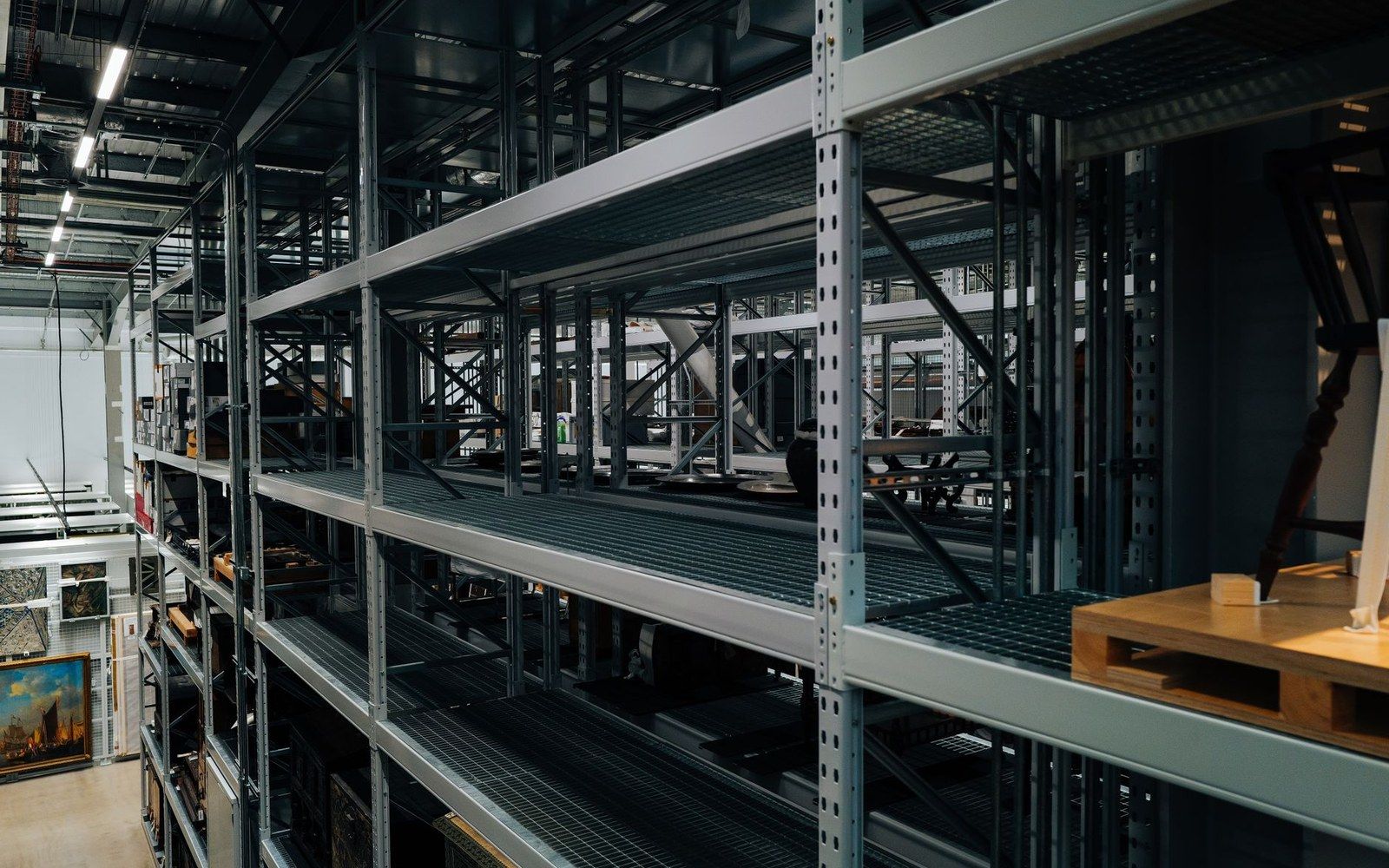Rows of metal warehouse shelving hold framed paintings and stored artwork